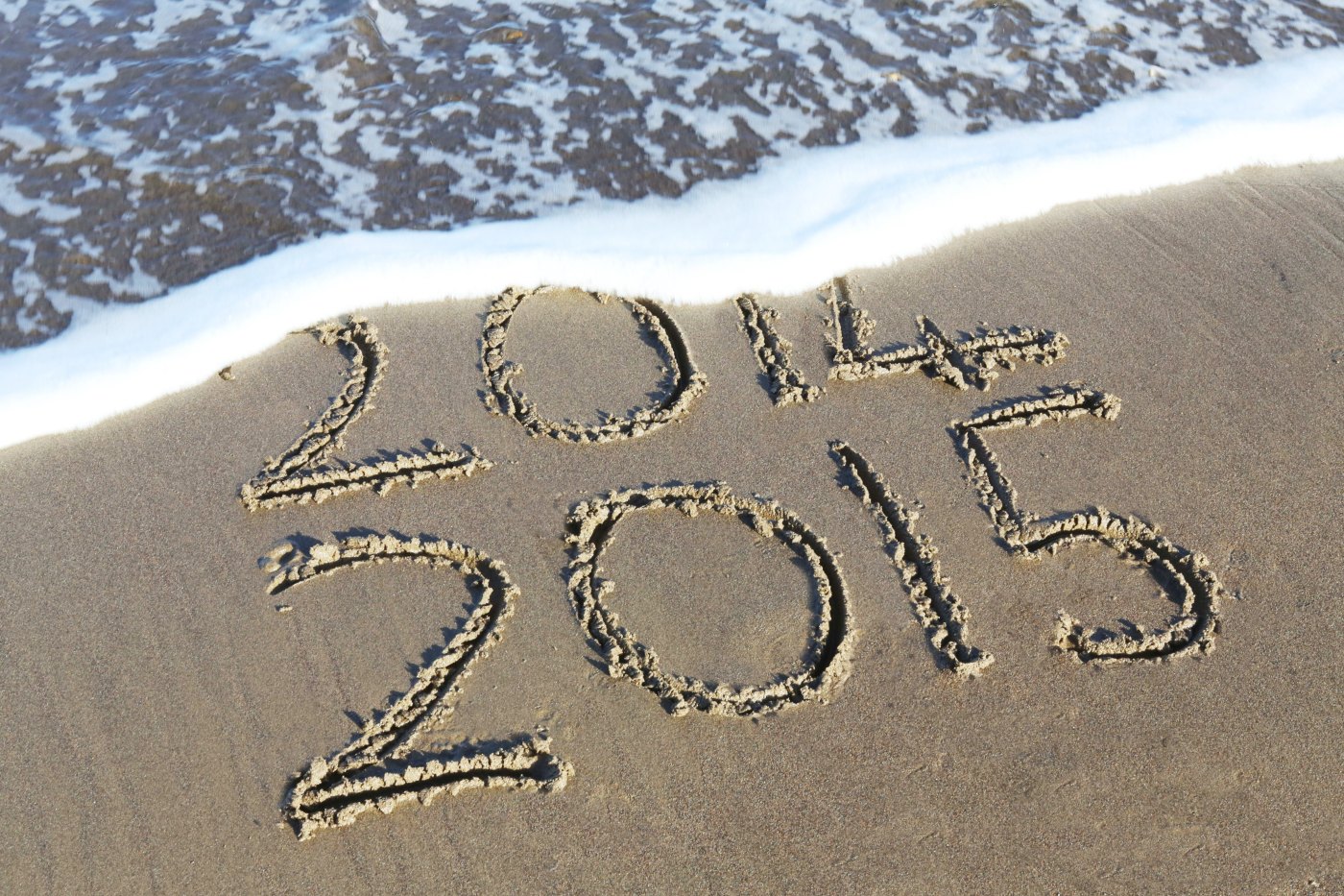ocean wave washing away part of the years 2014 and 2015 that are written in sand representing a positive office culture for the new year ahead