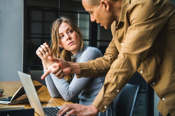 office manager pointing to a laptop screen talking with an employee who is looking at him with a serious face recognizing the importance of training managers to be mediators