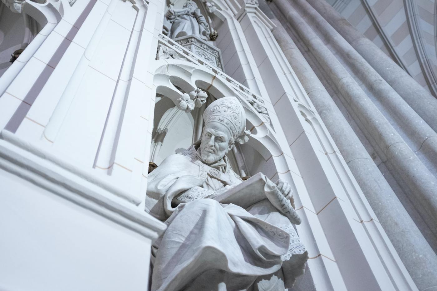 Marble statue carved out of a building of priest staring down upon the onlooker
