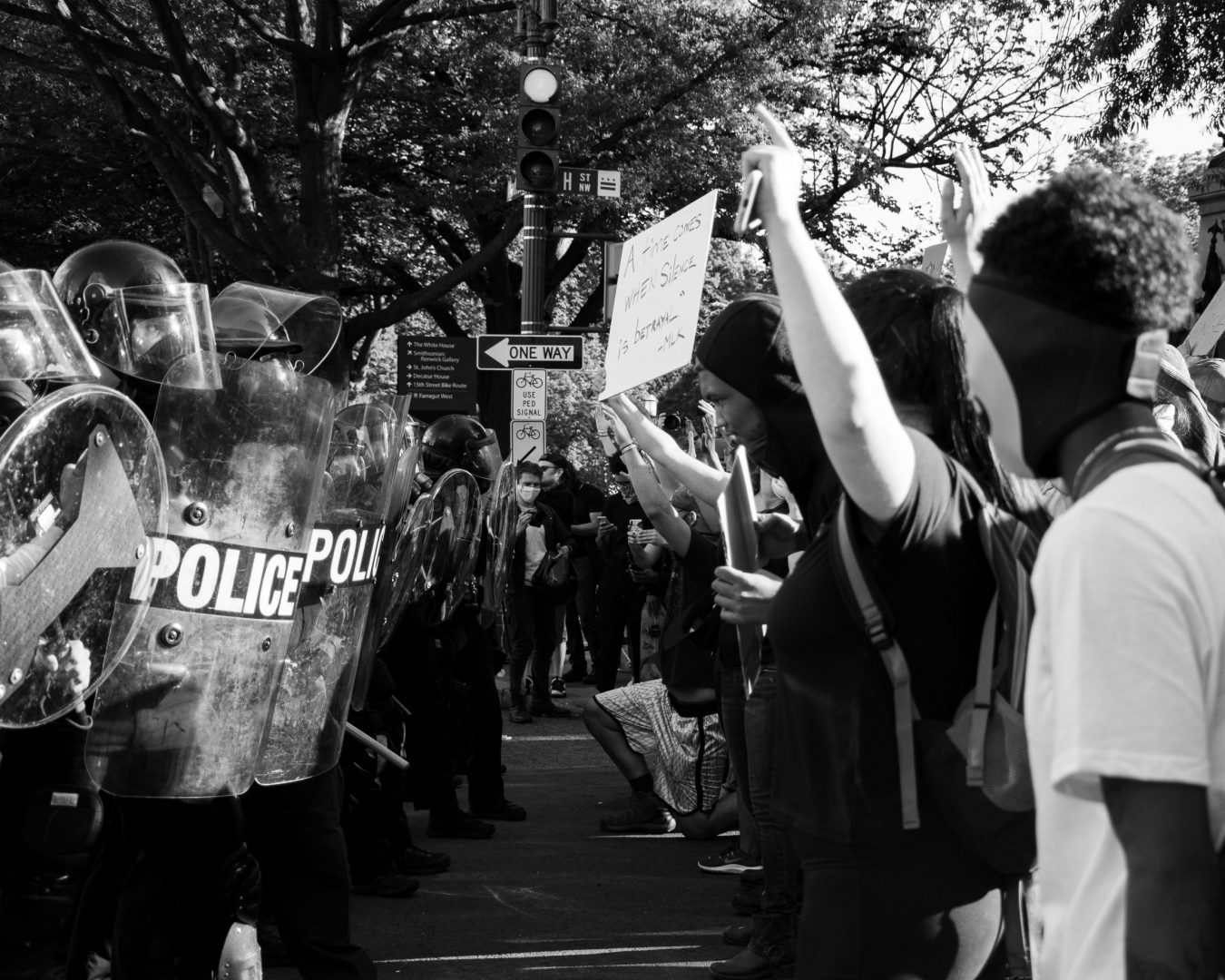 Black and white image of police in riot gear facing protestors on city street